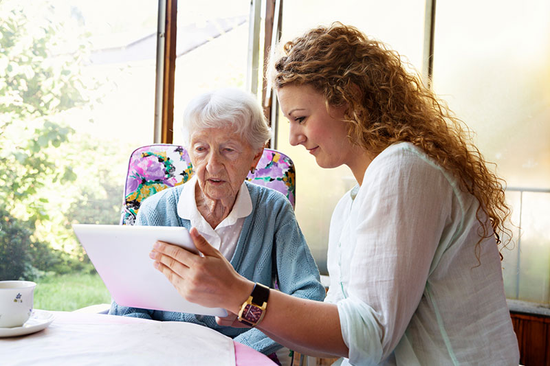 caregiver showing elderly woman laptop