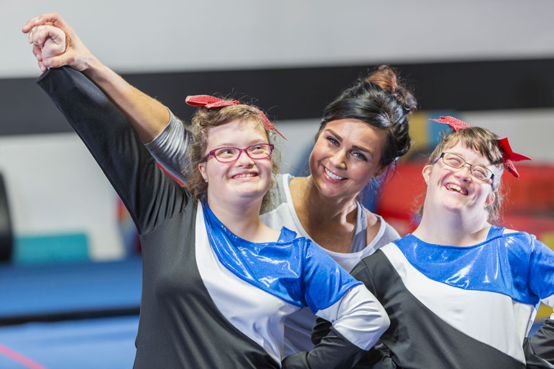 woman working with two developmentally disabled women in a gym